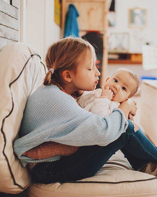 Schwester mit Baby auf Sitzkissen beige